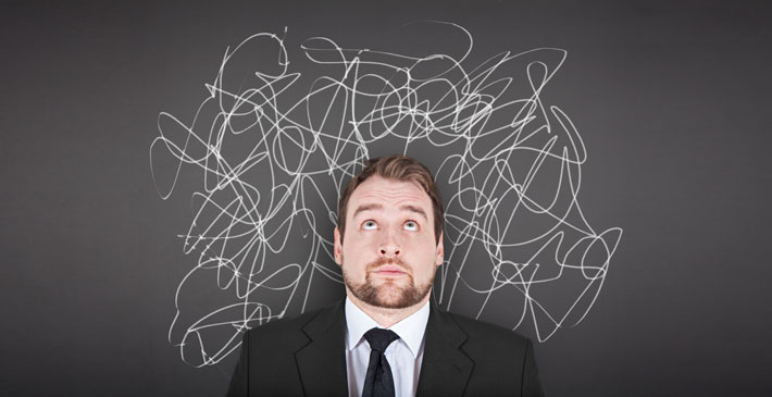 Man standing in front of chalk board looking up with squiggly lines on the board behind his head