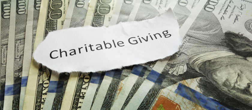 A hundred dollar bills in the background with charitable giving on a piece of paper