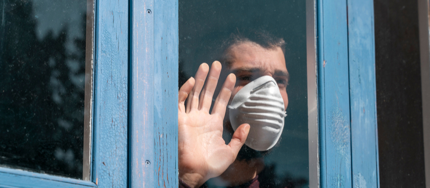 A man with a mask on holding his hand on the glass